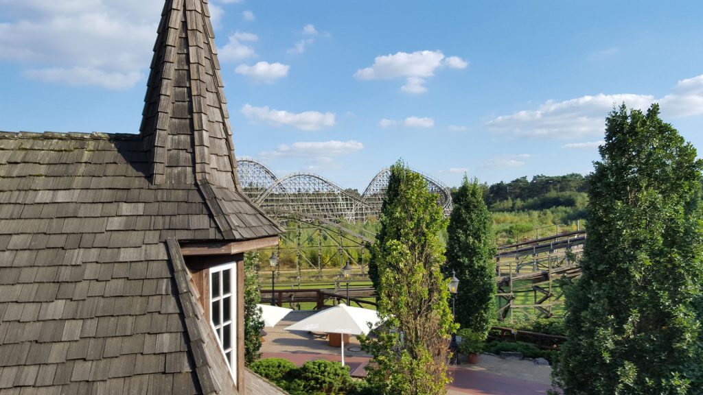 Achterbahn Colossos liegt versteckt hinter Gebäuden und Bäumen